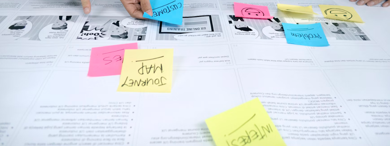 Hands arranging colourful sticky notes with labels like "Customer," "Problem," and "Journey Map" on a UX design canvas during a collaborative planning session.